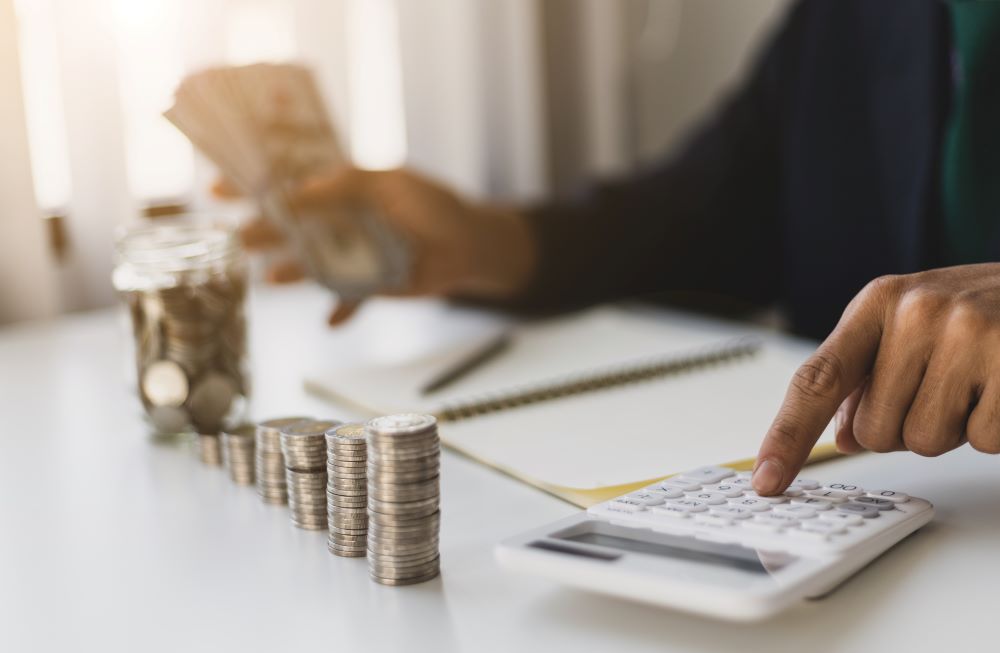 Close up of a person calculating something with a stack of coins in front of him