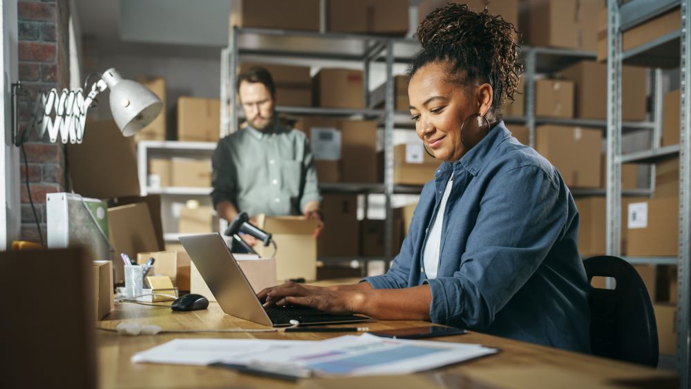 Women typing on a laptop while man at the background packing a box